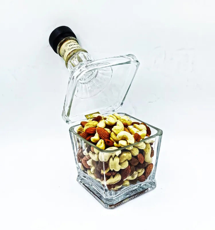 Upcycled Jack Daniel's Glass Bottle Canister filled with mixed dry fruits (almonds, cashews, etc.). Square glass jar with the bottle neck as a lid, clear glass showing contents. Unique serving and eco-friendly home decor."