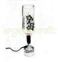 Indri printed bottle table lamp switched on beside a bed, casting warm light over a nightstand with books